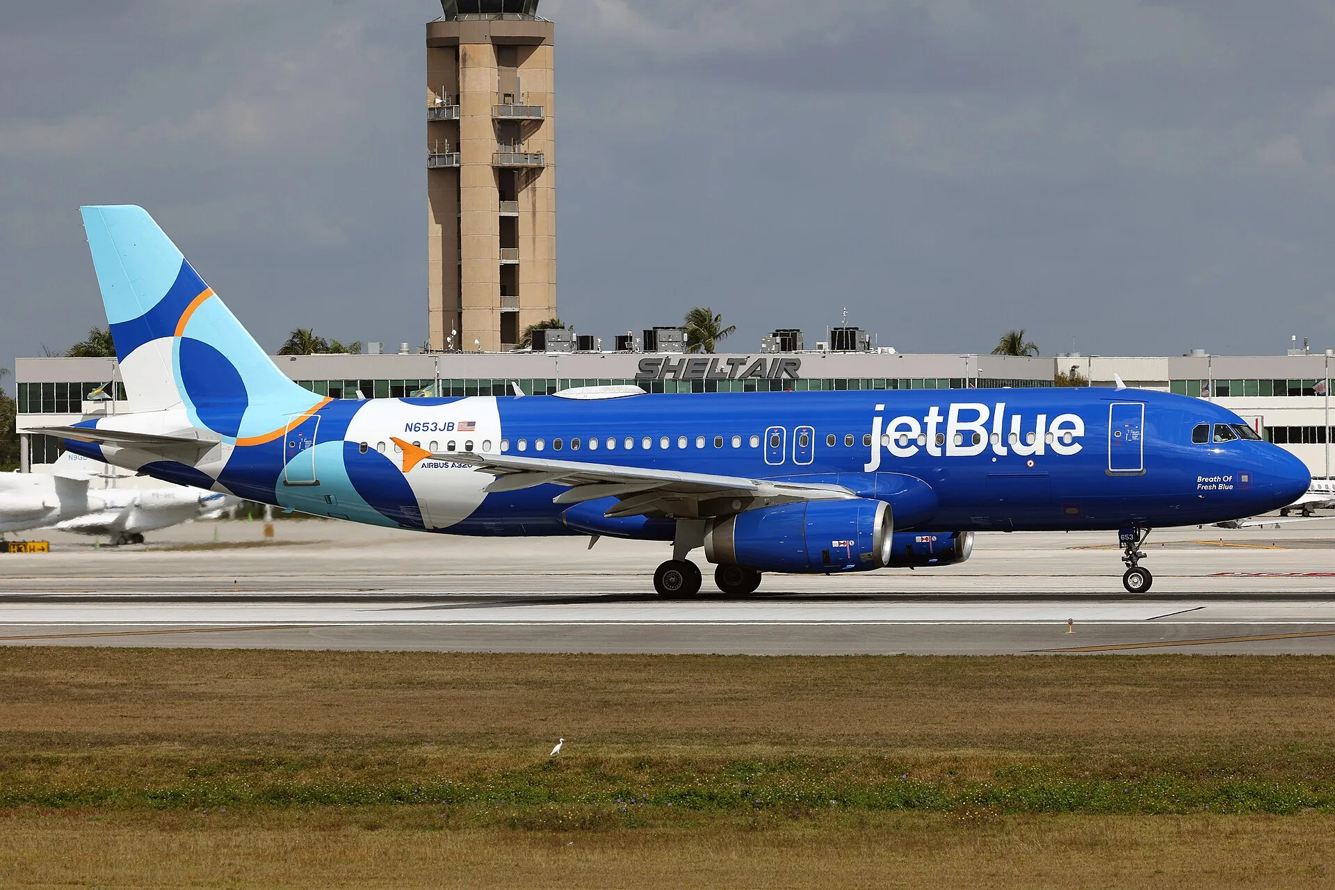 A JetBlue Airbus A320 on the runway at Fort Lauderdale-Hollywood International Airport, with the control tower behind.